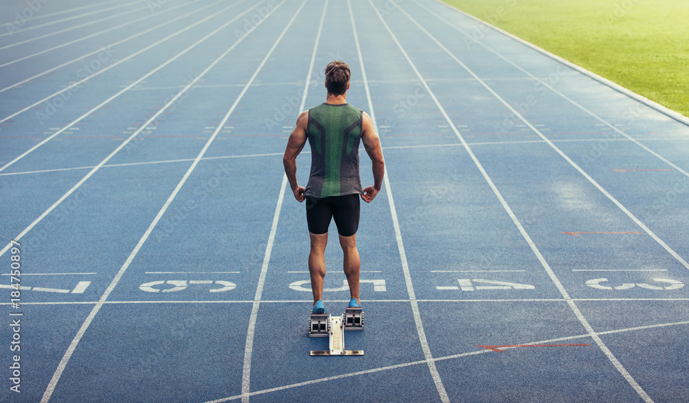 Wall mural sprinter standing on starting block on running track
