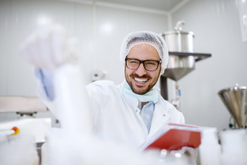 Close up of cheerful focused professional happy scientist man holding clipboard and white bottle in...