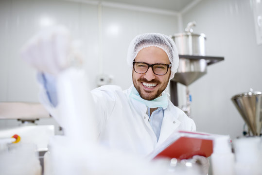Close up of cheerful focused professional happy scientist man holding clipboard and white bottle in the laboratory room.