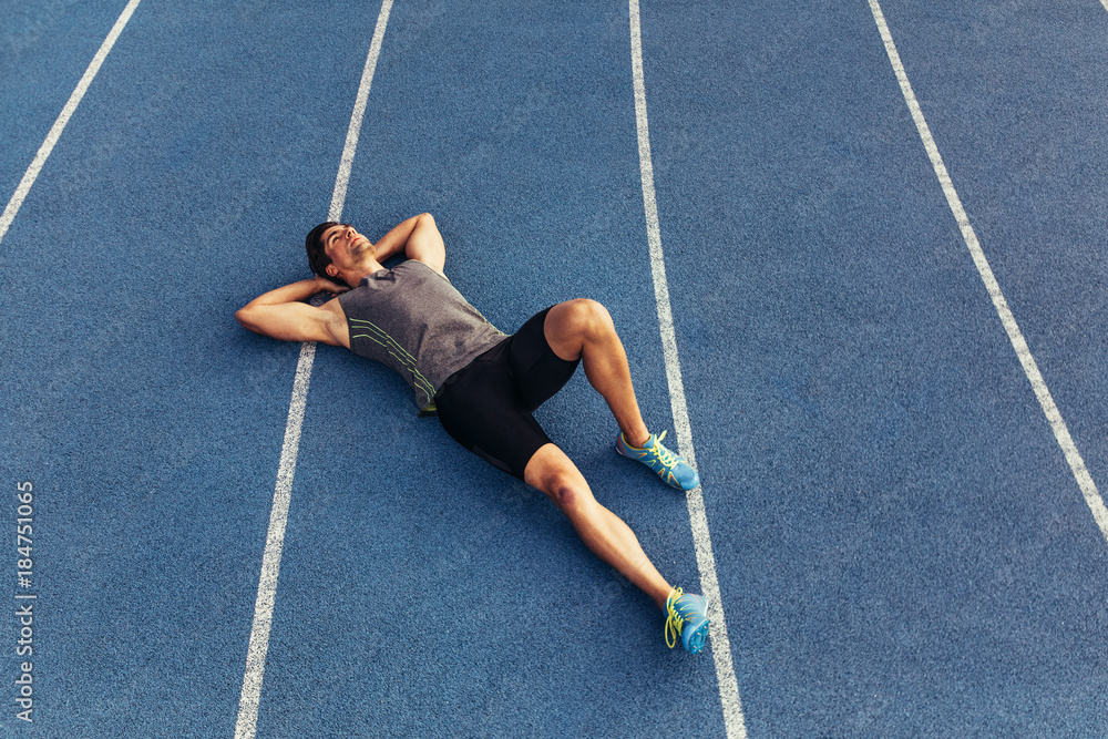 Wall mural sprinter relaxing by lying on the running track