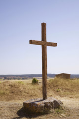 cruz símbolo religioso cristiano de madera en medio de un camino sujeta por dos grandes piedras en un campo cerca de la carretera bajo el cielo azul