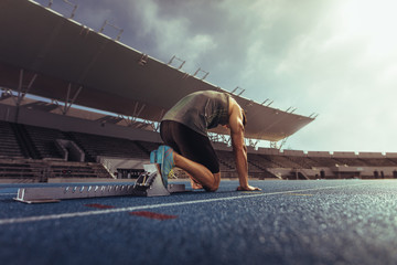 Sprinter resting his feet on a starting block on running track