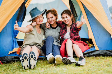Happy three Asian girl friends smiling and show thumb up outside tent on vacation holiday. teavel with friends concept