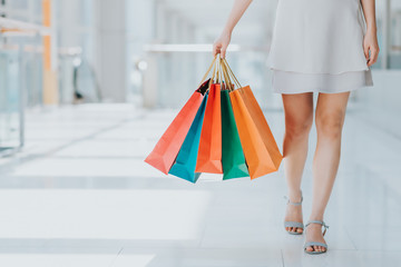 Close up shot of young woman leg carrying colorful shopping bags while walking in shopping mall