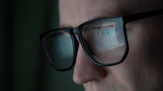 an office worker sits at the computer, a monitor with tables and graphs is reflected in the glasses.