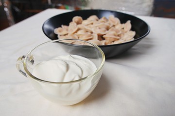 Traditional dish of dumplings in a bowl on a white tablecloth. Served with sour cream, a fork and a spoon.