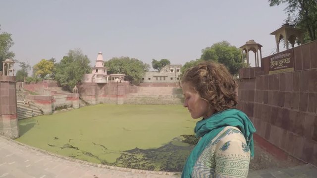 Caucasian woman walks steps by sacred traditional stone bathing pond in India, stops and folds her hands in prayer, smooth tracking shot, wide angle.mov
