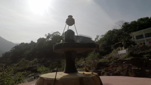]Shiva Lingam rotating tracking shot with Ganges River, hills and mountains in background. Rishikesh, India. 2X slow motion. Mid shot.