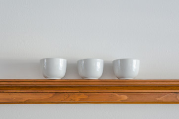 Three symetrical white saki cups on a wooden pine shelf