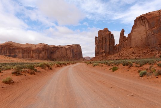 Red Desert Valley Road - A unpaved dirt road winding through red sandstone desert valley in the famous Monument Valley, Utah & Arizona, USA.