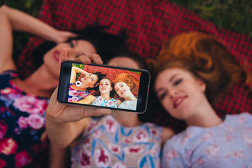 Group of women making selfie on smartphone, lay on grass during picnic