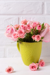 Pink roses flowers in green cup against  white brick wall.