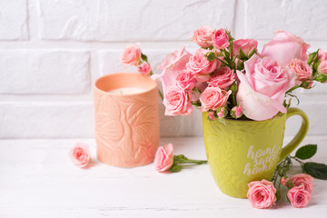 Pink roses flowers in green cup  and candle against  white brick wall.