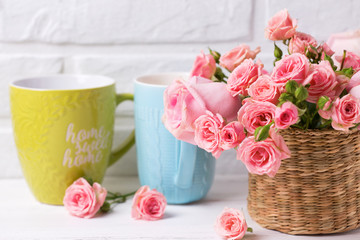 Pink roses flowers  and  colorful  green and blue cups against  white brick wall.