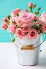 Bunch of tender pink roses flowers in pot against turquoise wall.