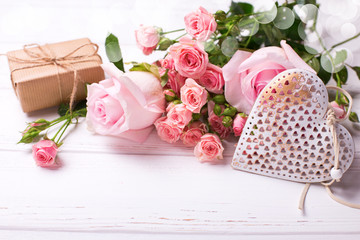 Tender pink roses flowers, decorative heart and  box with present on white wooden background.