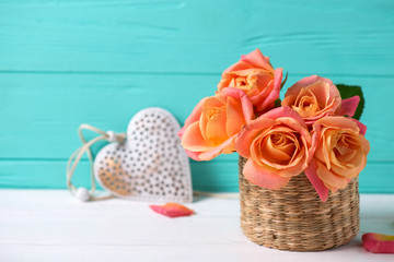 Fresh orange roses and heart on white wooden background against turquoise wall.