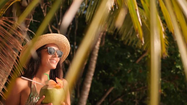 Young Attractive Mixed Race Tourist Girl Drinking Fresh Thai Coconut Water at Tropical Beach. 4K, Slowmotion. Phuket, Thailand.