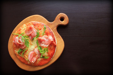 Pizza with smoked ham and rucola on dark background