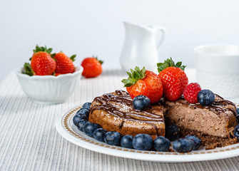 Big chocolate cheesecake with blueberry strawberry raspberry on a round plate.