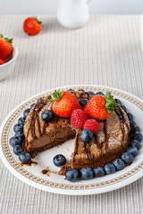 Big chocolate cheesecake with blueberry strawberry raspberry on a round plate.