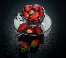Fresh strawberries in a glass cup on black glass