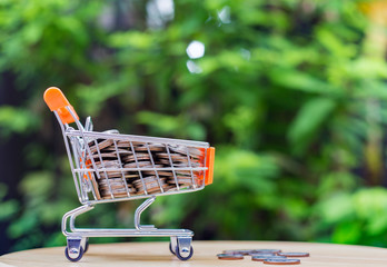 A Shopping cart full with coin stacked on green background