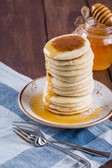 high stack of pancakes with honey on a white plate and a wooden background