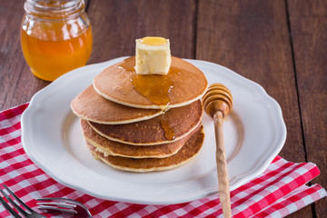 stack of pancakes with butter and honey on a white plate and a wooden background