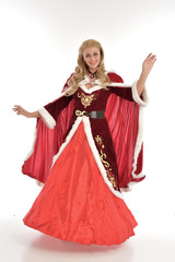 Obraz na płótnie Canvas full length portrait of pretty blonde lady wearing red and white christmas inspired costume gown, standing pose on white background.