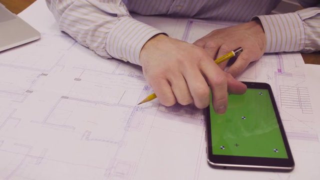 Close up. High angle view the architect's hands correcting the drawing and scrolling a tablet with green screen