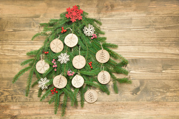 Christmas tree maked of spruce branch decorated wooden slice, snowflakes, holly berries on wooden...