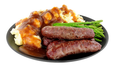 Fried venison sausages meal with mashed potatoes and asparagus on a black plate isolated on a white background