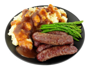 Fried venison sausages meal with mashed potatoes and asparagus on a black plate isolated on a white background