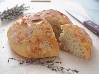 Freshly baked bread with thyme sprig upon cutting board. One piece is cut. Homemade bread. Selective focus.