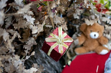 decorative red little gift as ornament on oak Christmas tree, traditional orthodox decoration with bear toy in background
