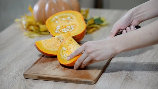 Woman cleaning pumpkin on wooden kitchen table. Male preparing to cutting orange pumpkin piece.