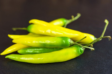 Pile of yellow and green peppers on black stone slab.