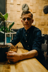 Portrait of handsome young man in a hat. He is in of darkroom coffee shop background. Confident and trendy look.