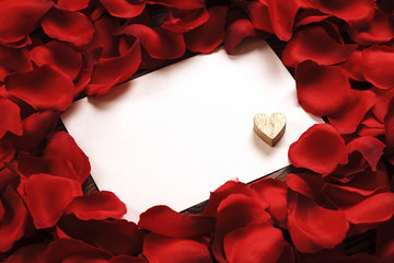 White blank card in red roses petals with golden wooden heart close up, copy space. Valentines day, love letter, wedding invitation concept