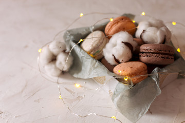Gift box with french macaroons and cotton flowers on white background with lights, copy space