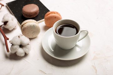 French macaroons with coffee cup, notebook, envelope and cotton flowers on white table