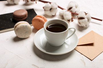 French macaroons with coffee cup, notebook, envelope and cotton flowers on white table