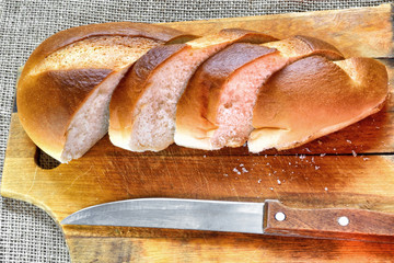 The bread cut by pieces and knife on a wooden chopping board.