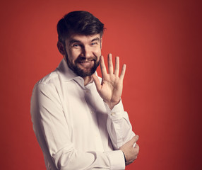 Happy smiling bearded businessman waving the hand and saying hello in fashion white style shirt on red background. Closeup toned portrait