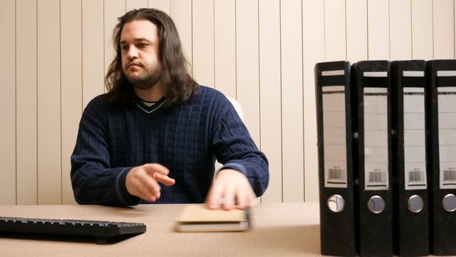 Long-haired businessman in his office is working on a computer and has a hysteria crisis because of too much work. Dolly shot. The man is bouncing his head