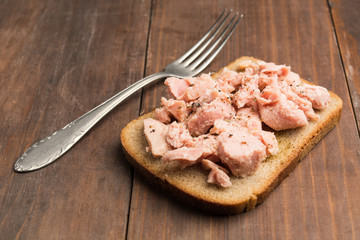 Bread with red fish preserve with fork on wooden table