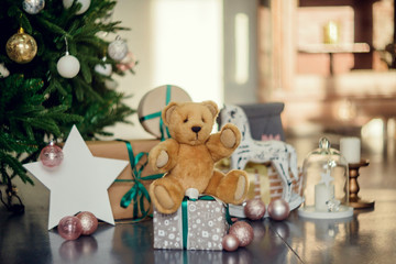 Cute little boy sitting down by the decorated Christmas tree with toys, teddy bears and gift boxes