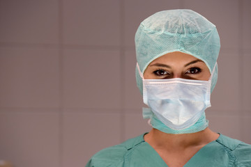 A young woman poses  in an operation theater  fully dressed as a theater nurse with a face mask  and green sterile medical work clothing.