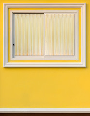 White frame window in yellow wall with curtain.